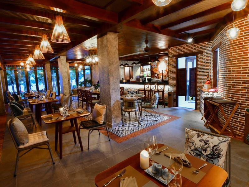 Gemütliches Restaurant mit Holzbalken, warmem Licht, Tischen, Stühlen und einer Bar im Hintergrund.