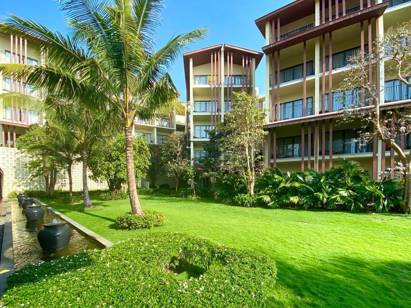 Grüne Gartenfläche mit Palmen und modernen mehrstöckigen Gebäuden bei klarem Himmel.
