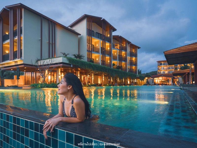 Frau im Pool bei Dämmerung vor beleuchtetem, mehrstöckigem Hotel mit moderner Architektur.