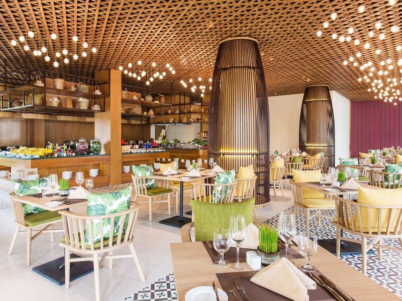 Modernes helles Restaurant mit Holzdecke, vielen Lampen und farbigen Stühlen an Tischen.