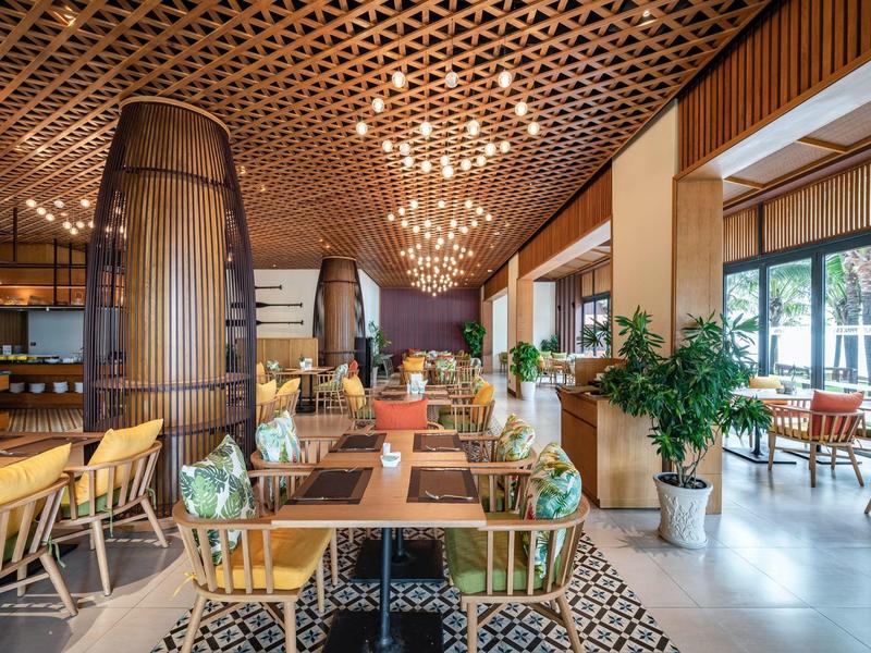 Modern eingerichteter Speisesaal mit Holzmöbeln, Pflanzen und Deckenbeleuchtung.