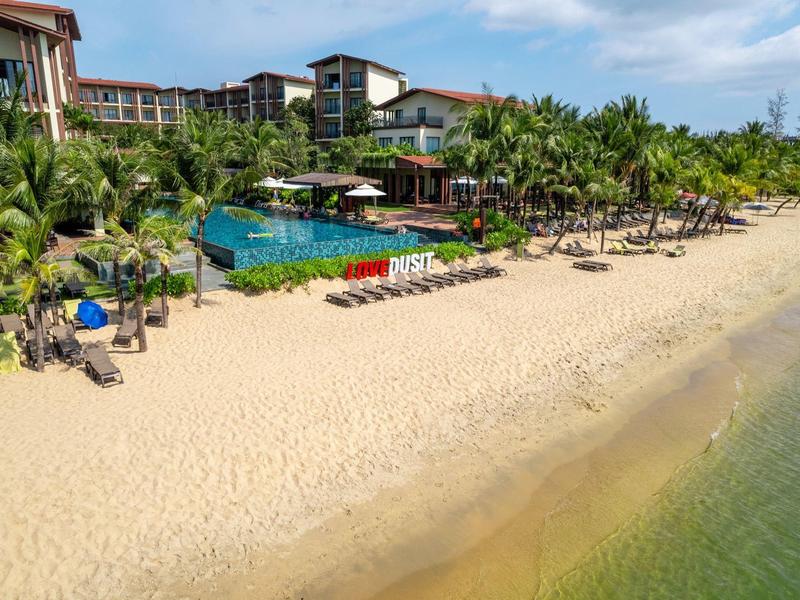 Hotelresort mit Pool, Palmen und Strandliegen an einem ruhigen Sandstrand.