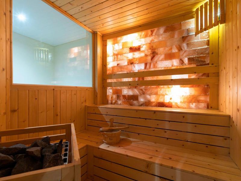 Moderne Sauna mit Holzbänken und beleuchtetem Salzsteinwand-Design, warmes gelbliches Licht.