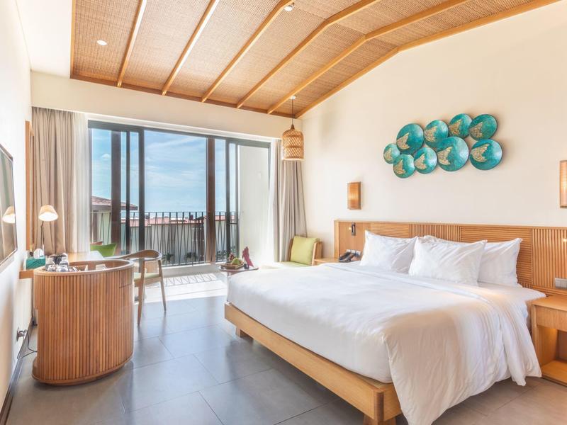 Helles Hotelzimmer mit Doppelbett, Schreibtisch und Balkon mit Meerblick.