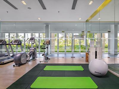 Moderner Fitnessraum mit Laufbändern, Trainingsgeräten, grüner Matte und großer Glasfront mit Blick ins Freie.