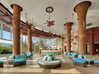 Großer, heller Raum mit runden Sofas, hohen Säulen und Panoramafenstern mit Außenblick.