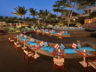 Gemütliche Terrasse mit blauen Sitzpolstern, Holztischen und weißen Stühlen bei Abenddämmerung.