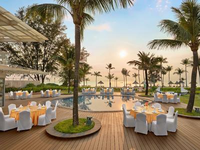 Elegante Außenbestuhlung mit rundem Pool und Palmen in einem tropischen Resort bei Sonnenuntergang.