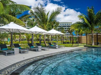 Hotelpool mit Liegestühlen und Sonnenschirmen umgeben von Palmen und Hotelgebäuden.