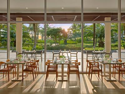 Hell eingerichteter Speiseraum mit Blick auf eine grüne Gartenanlage bei Sonnenuntergang.