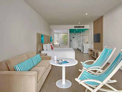 Moderner Wohnbereich mit Sofa, zwei Liegestühlen, Tisch und durchsichtiger Trennwand zum Schlafzimmer.