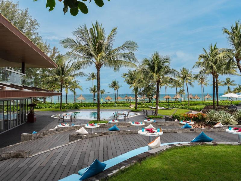 Moderner Poolbereich mit Liegen, Palmen und Blick auf das blaue Meer unter klarem Himmel.