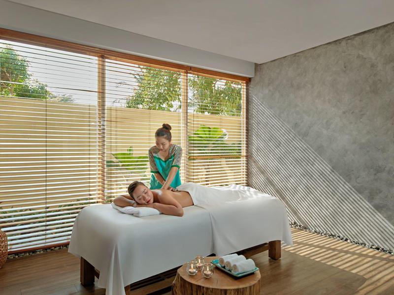 Frau massiert liegenden Mann in hellem Raum mit großen Fenstern und Holzboden.