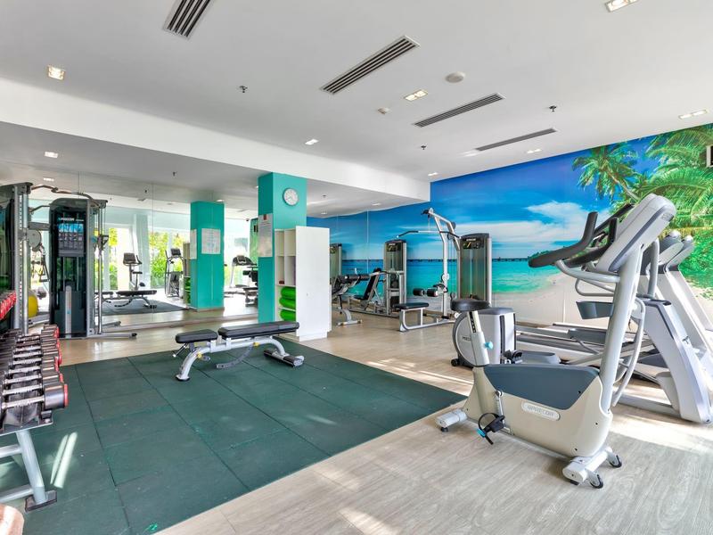 Moderner Fitnessraum mit Geräten, Hanteln, Spiegeln und Wandmalerei eines tropischen Strandes.