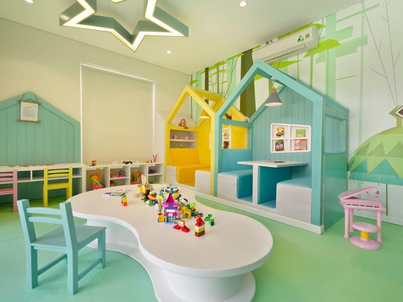 Buntes Kinderzimmer mit kleinen Häusern, ovalem Tisch, Stühlen und kreativem Spielzeug.