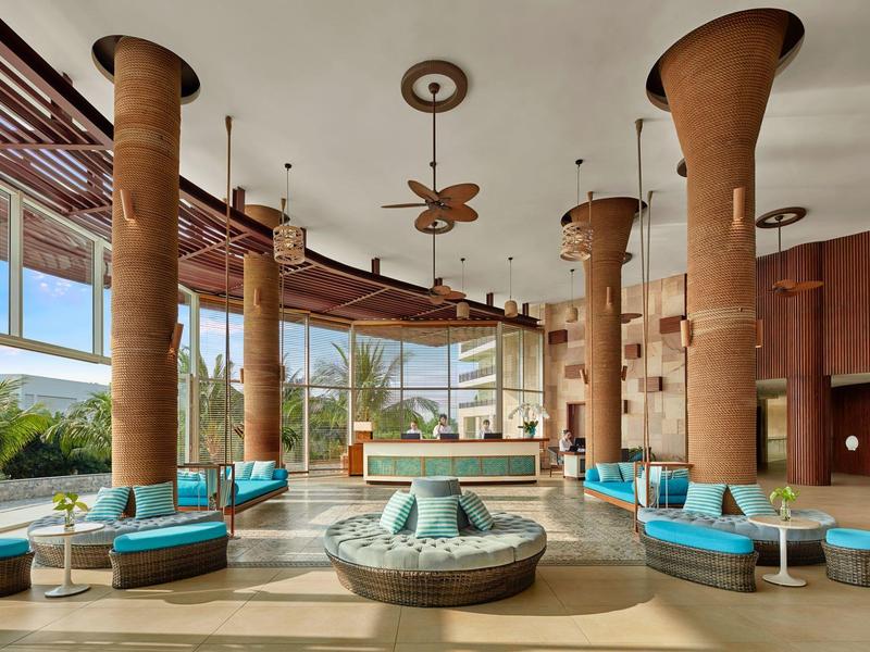 Großer, heller Raum mit runden Sofas, hohen Säulen und Panoramafenstern mit Außenblick.