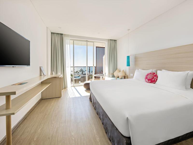 Helles Hotelzimmer mit großem Bett, Holzfußboden, Balkon und Meerblick.