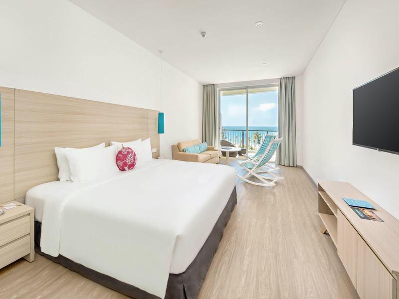 Helles Hotelzimmer mit großem Bett, Holzboden, Balkon und Meerblick, moderner Einrichtung.