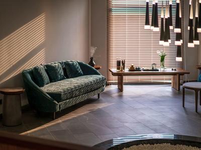 Gemütliches Wohnzimmer mit grünem Sofa, Holztisch, Stühlen und modernem Kronleuchter bei Abendlicht.