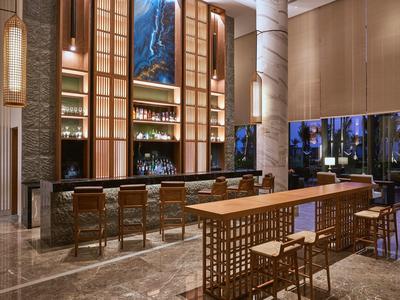 Moderner Hotelbarbereich mit hohem Deckengewölbe, beleuchtetem Tresen und Holzstühlen in hellem Ambiente.