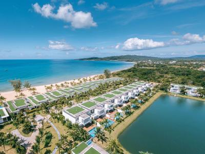 Luxuriöse Villen mit privaten Pools neben einem Sandstrand und einem See unter blauem Himmel