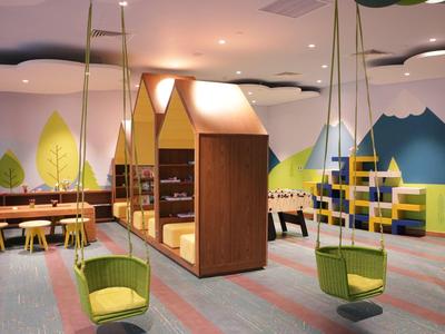 Kindgerechter Raum mit gelben Schaukelsitzen, Holzhaus-Modul und farbiger Wanddekoration.