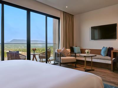 Helles Hotelzimmer mit großem Bett, Sofa, Tisch, Fernseher und Terrasse mit Meerblick.