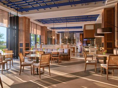 Geräumiges Hotelrestaurant mit modernen Holzmöbeln und großen Fenstern mit Blick auf Palmen.