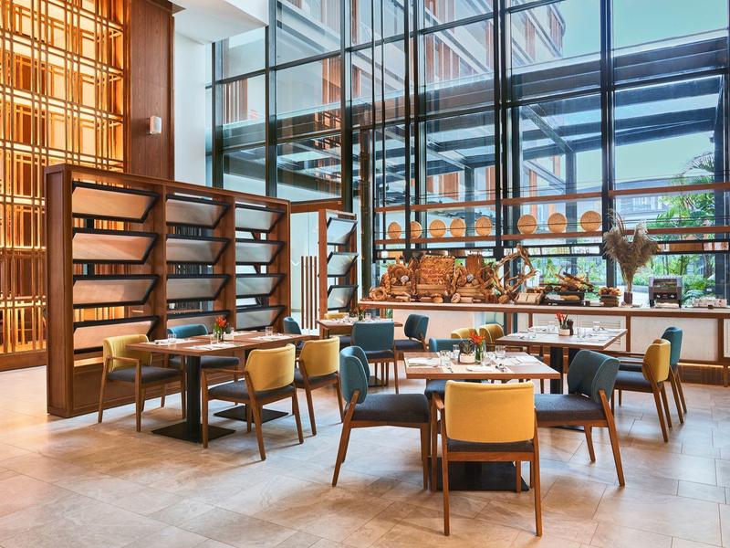 Moderner Hotelrestaurantbereich mit Tischen, Stühlen und großen Fenstern mit Blick ins Freie.