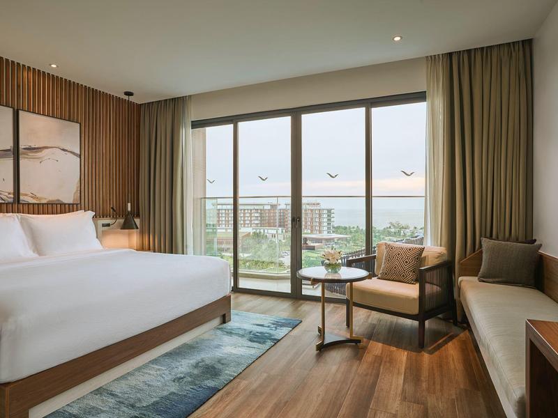 Modernes Hotelzimmer mit großem Bett, Sitzbereich und Blick auf Balkon und Meer