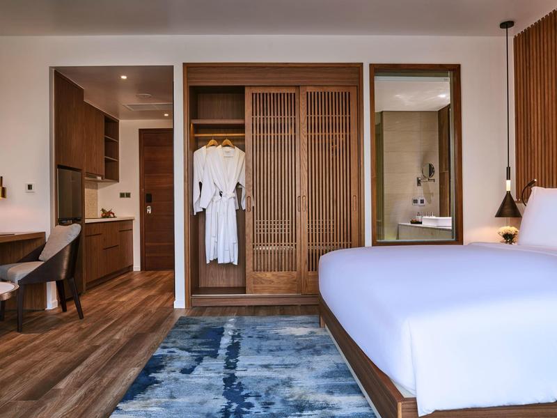 Modernes Schlafzimmer mit Holzmöbeln, blauem Teppich und offenem Kleiderschrank mit weißen Roben.