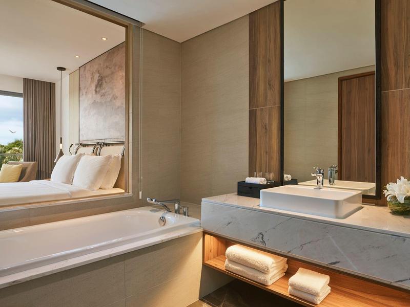 Modernes Badezimmer in Beige- und Holztönen mit großer Badewanne und Waschbecken auf Marmorplatte.