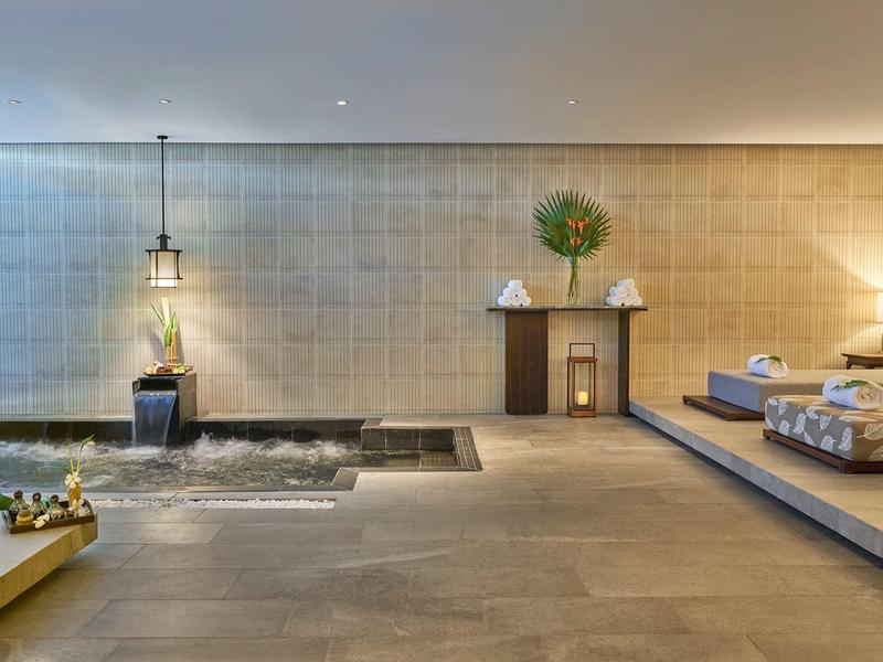 Modernes Zimmer mit großem Bett, Wasserbecken, Pflanzen und warmen Lampen an der Wand.