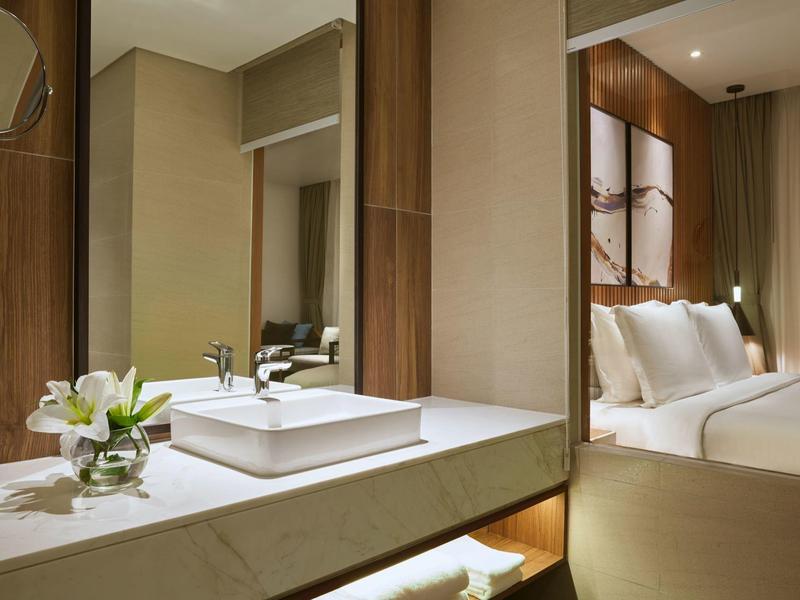 Moderner Badwaschtisch mit eckigem Waschbecken und Blumen, dahinter ein Schlafzimmer mit Bett und Kunst.