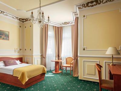Elegantes Hotelzimmer mit Doppelbett, grünem Teppich und klassischer Einrichtung.