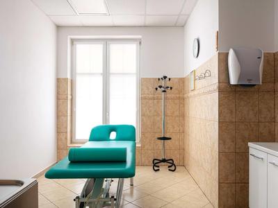 Brightly lit small medical examination room with green chair and window.