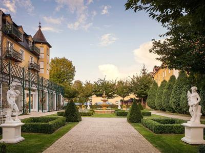 Eleganter Garten mit symmetrischen Hecken, Statuen und historischem Gebäude bei Sonnenuntergang.