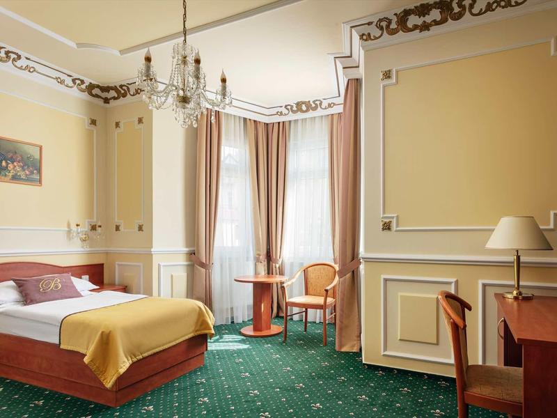 Elegant hotel room with double bed, green carpet, and golden curtains.