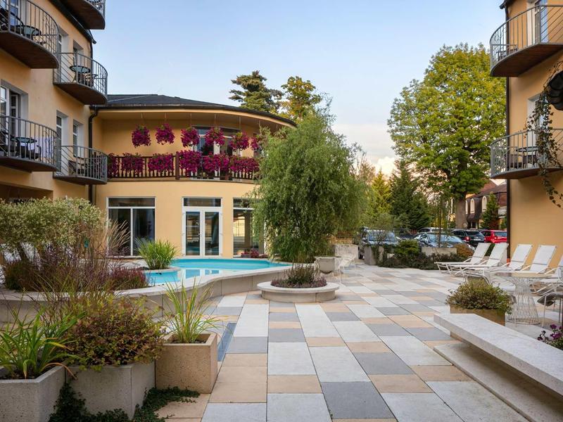 Hotel courtyard with swimming pool, seating areas, and flower arrangements under clear sky.