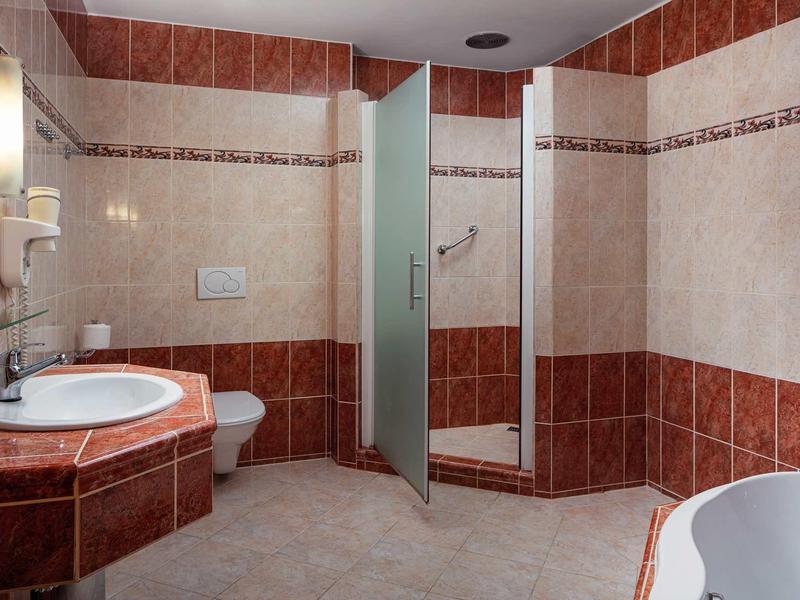 Modern bathroom with shower, toilet, sink, and bathtub in warm red tones.
