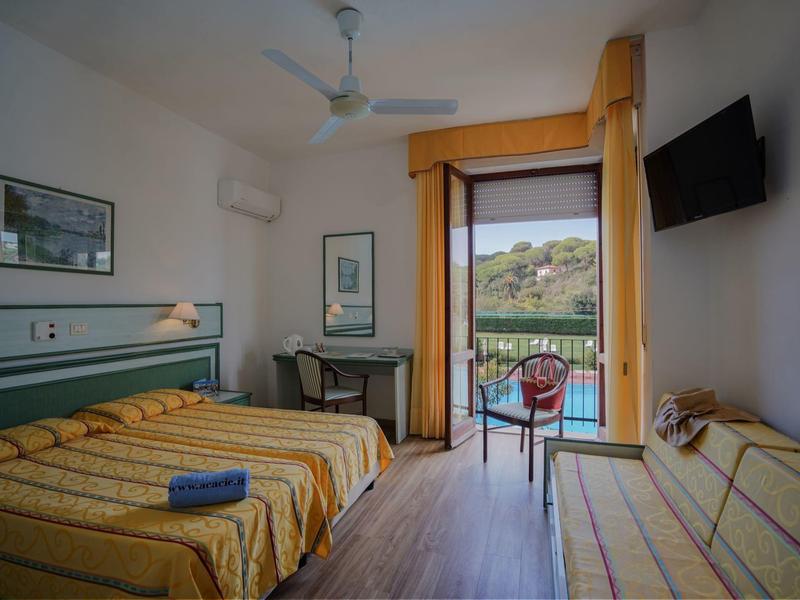 Hotelzimmer mit zwei Betten, einem Schreibtisch, Fernseher und Balkon mit Blick aufs Wasser.