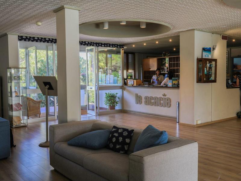 Helles Hotellobby mit Rezeption, Sofas und großem Fenster mit Blick nach draußen.