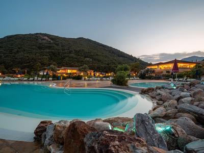 Pool mit türkisfarbenem Wasser am Abend nahe einem Hügel und Felsen im Vordergrund