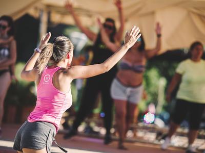 Frauen machen gemeinsam Fitnessübungen im Freien unter einem Sonnendach.