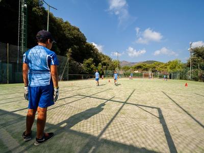 Ein Mann in blauem Sportoutfit steht auf einem Tennisplatz im Freien unter blauem Himmel.