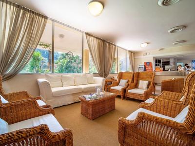 Heller Wohnraum mit Korbsesseln, weißem Sofa, Holztisch und großen Fenstern mit Vorhängen.