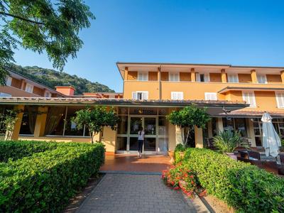 Mehrstöckiges gelbes Gebäude mit Veranda, grünen Hecken und sonnigem blauem Himmel.