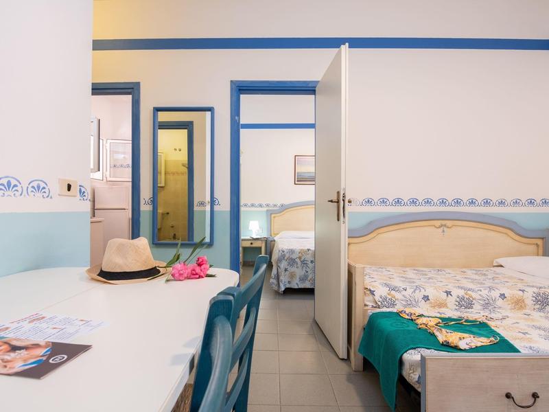 Zimmer mit Bett, Schreibtisch, Stuhl, offener Tür zum angrenzenden Raum, helle Wände, türkisfarbene Akzente.