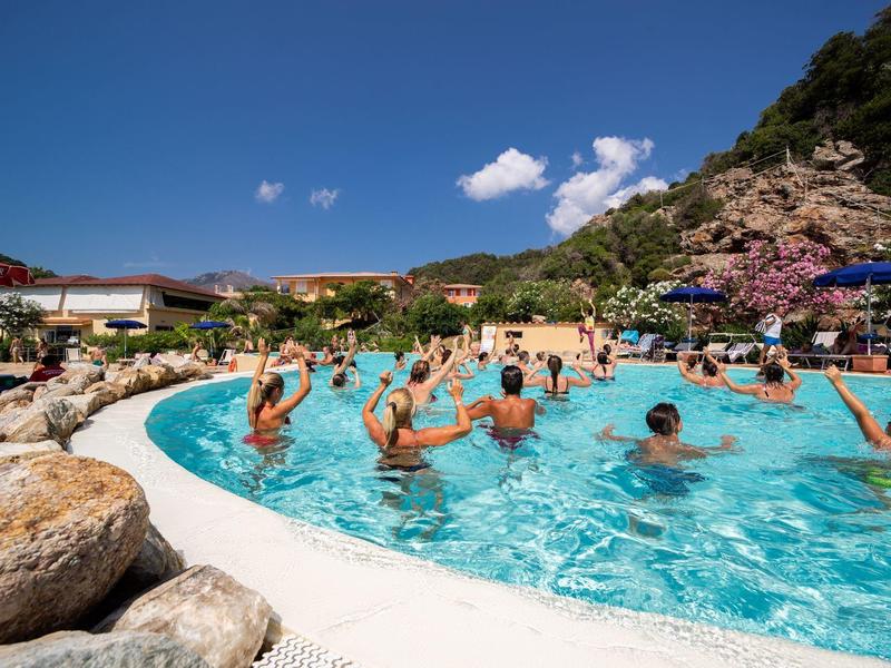 Menschen schwimmen und entspannen sich in einem runden Pool mit Bergen und blauem Himmel im Hintergrund.