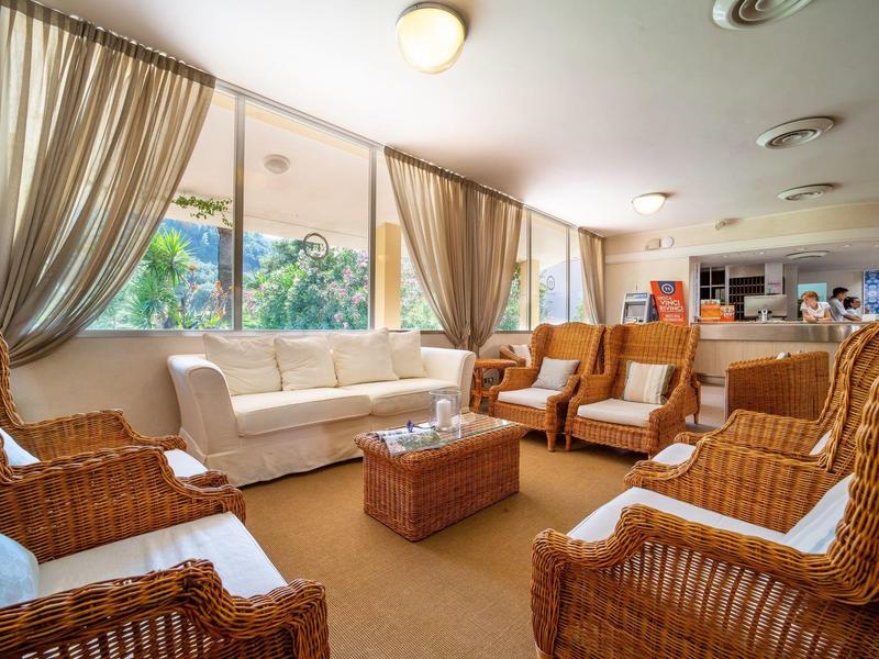 Heller Wohnraum mit Korbsesseln, weißem Sofa, Holztisch und großen Fenstern mit Vorhängen.